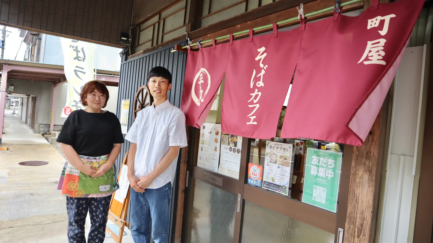 町屋 そばカフェ平丸の暖簾の前に立つクライアントと笠原 友生